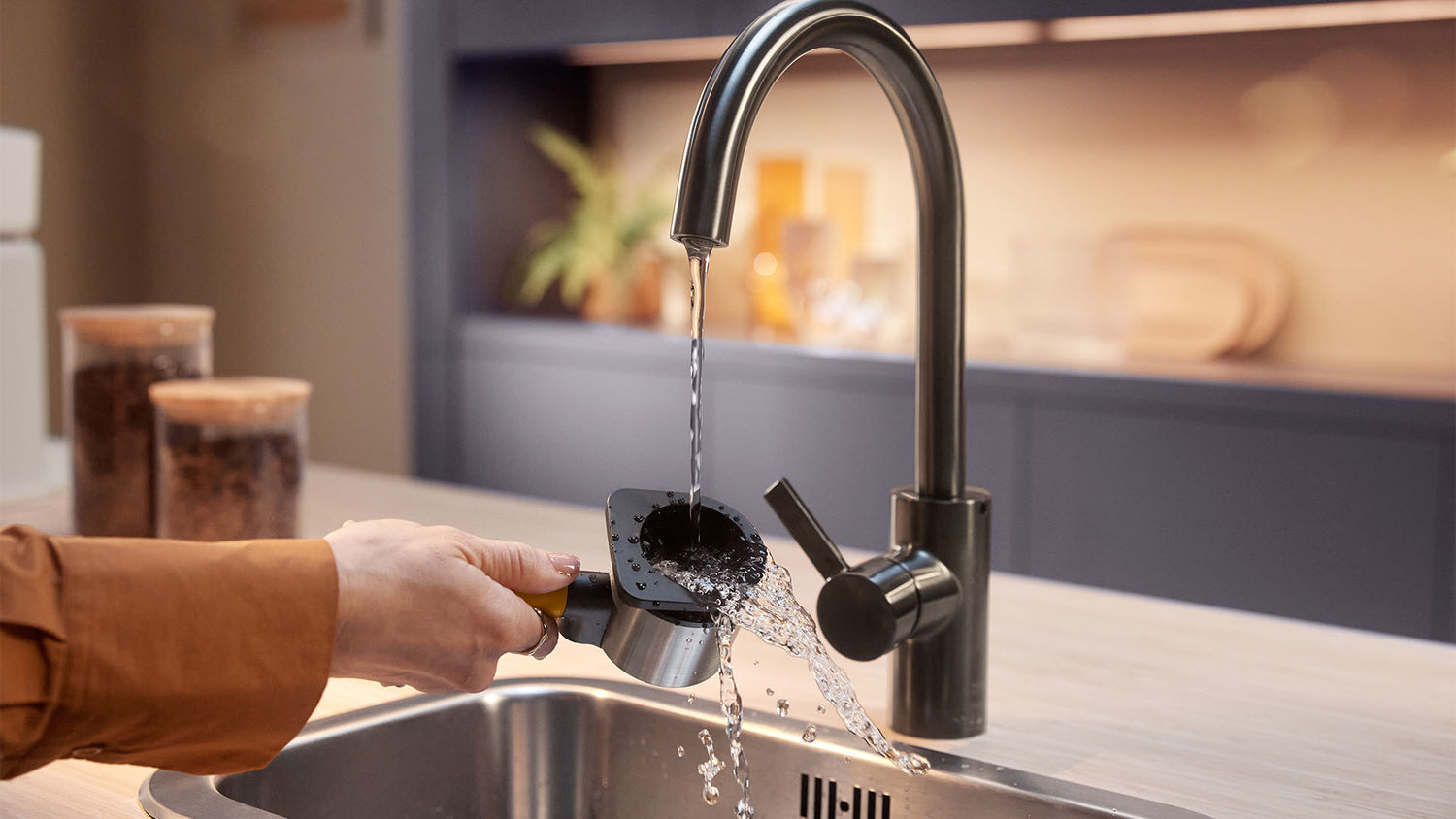 Close-up of a person rinsing a Philips coffee machine filter under a kitchen faucet.