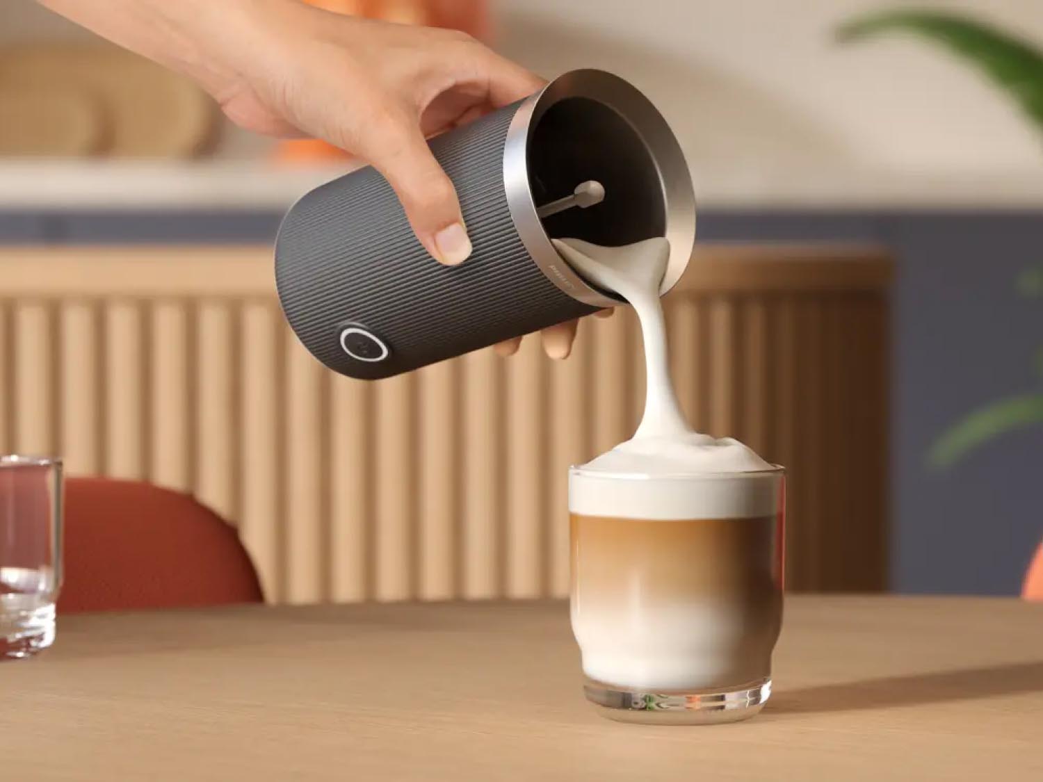 Close-up of a person pouring frothed milk into a cappuccino.