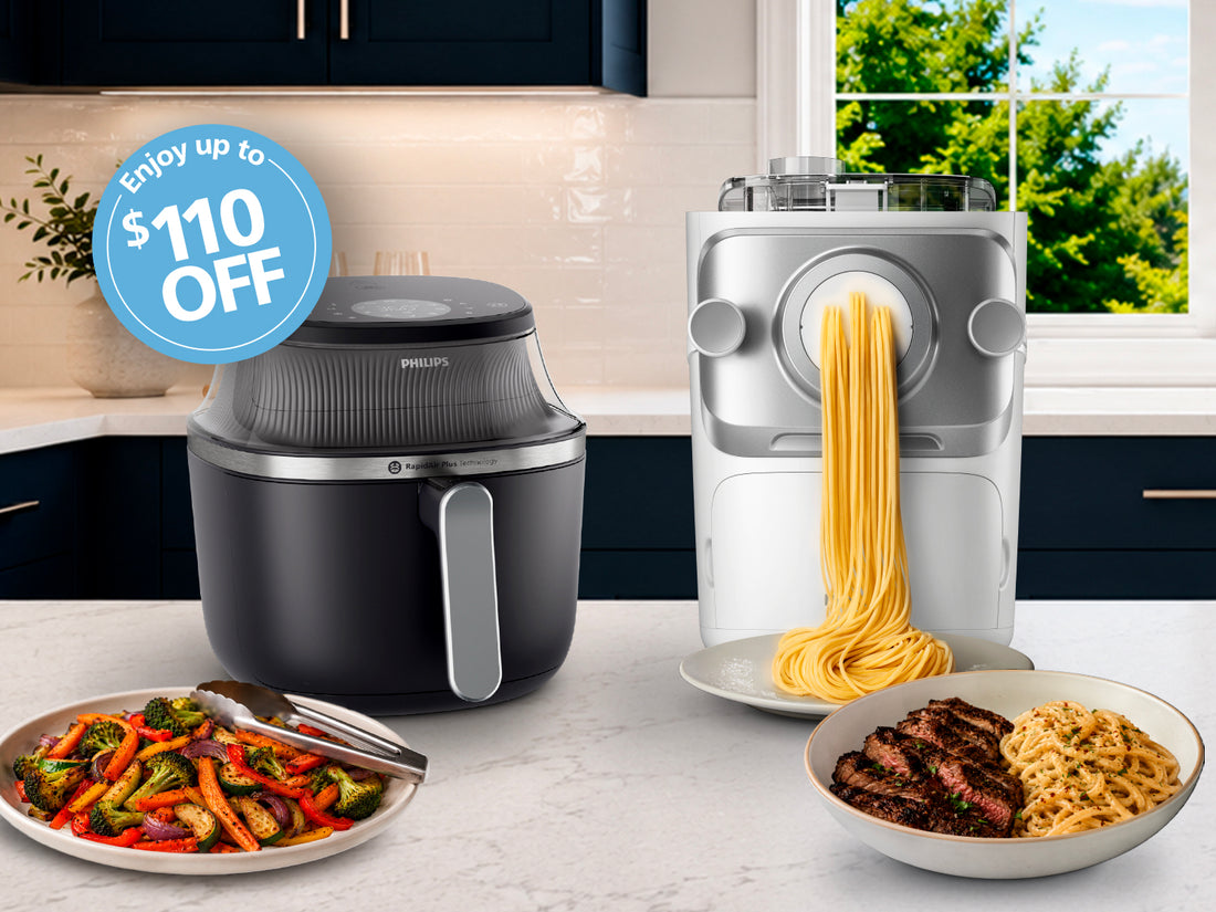 Kitchen scene with air fryer, pasta maker, and cooked food on a countertop.