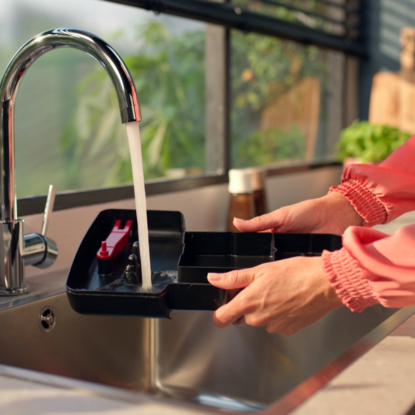 Person cleaning the coffee tray container with water at the kitchen sink.