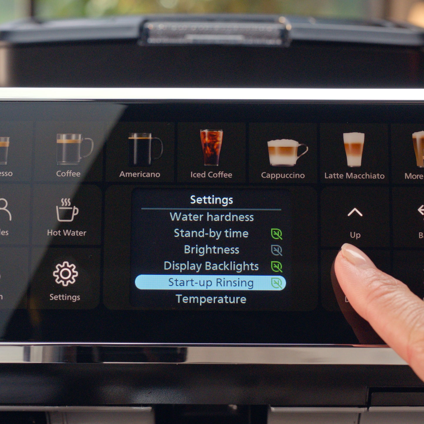 Coffee machine control panel with settings menu and a finger interacting with the screen.