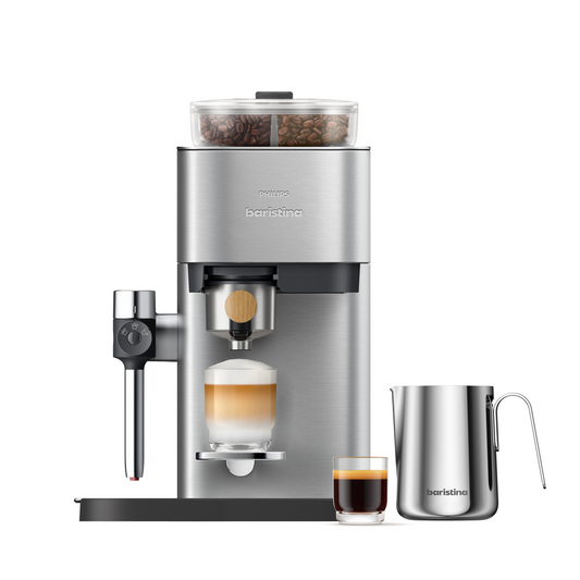 A Baristina Latte espresso machine in brushed stainless steel with a bean hopper on top, shown with a glass of layered latte, a small espresso cup, and a stainless-steel milk pitcher on a clean white background.