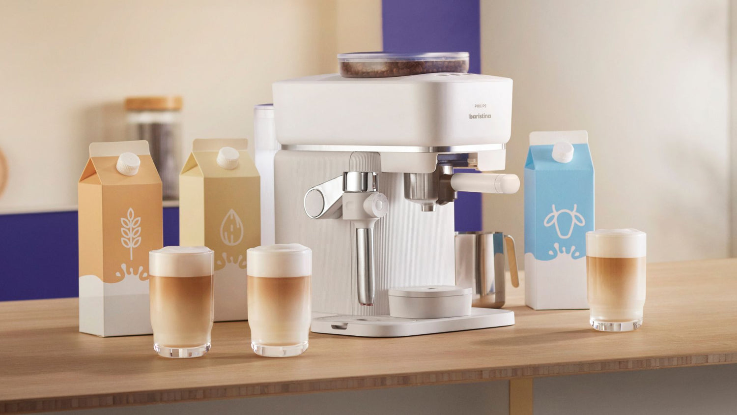 White coffee machine with glasses of coffee and milk cartons on a wooden surface.