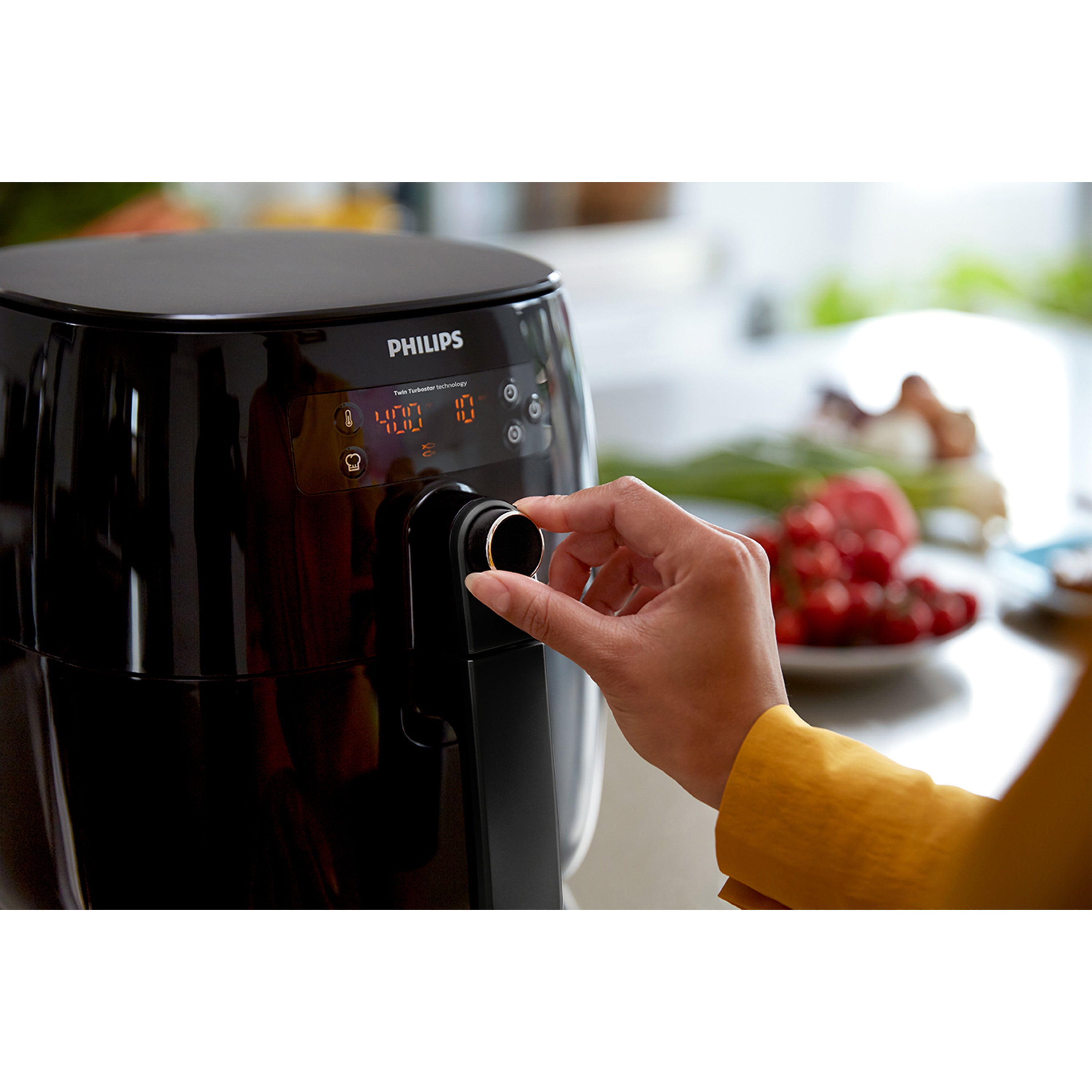 Person adjusting a Philips air fryer with a blurred kitchen background