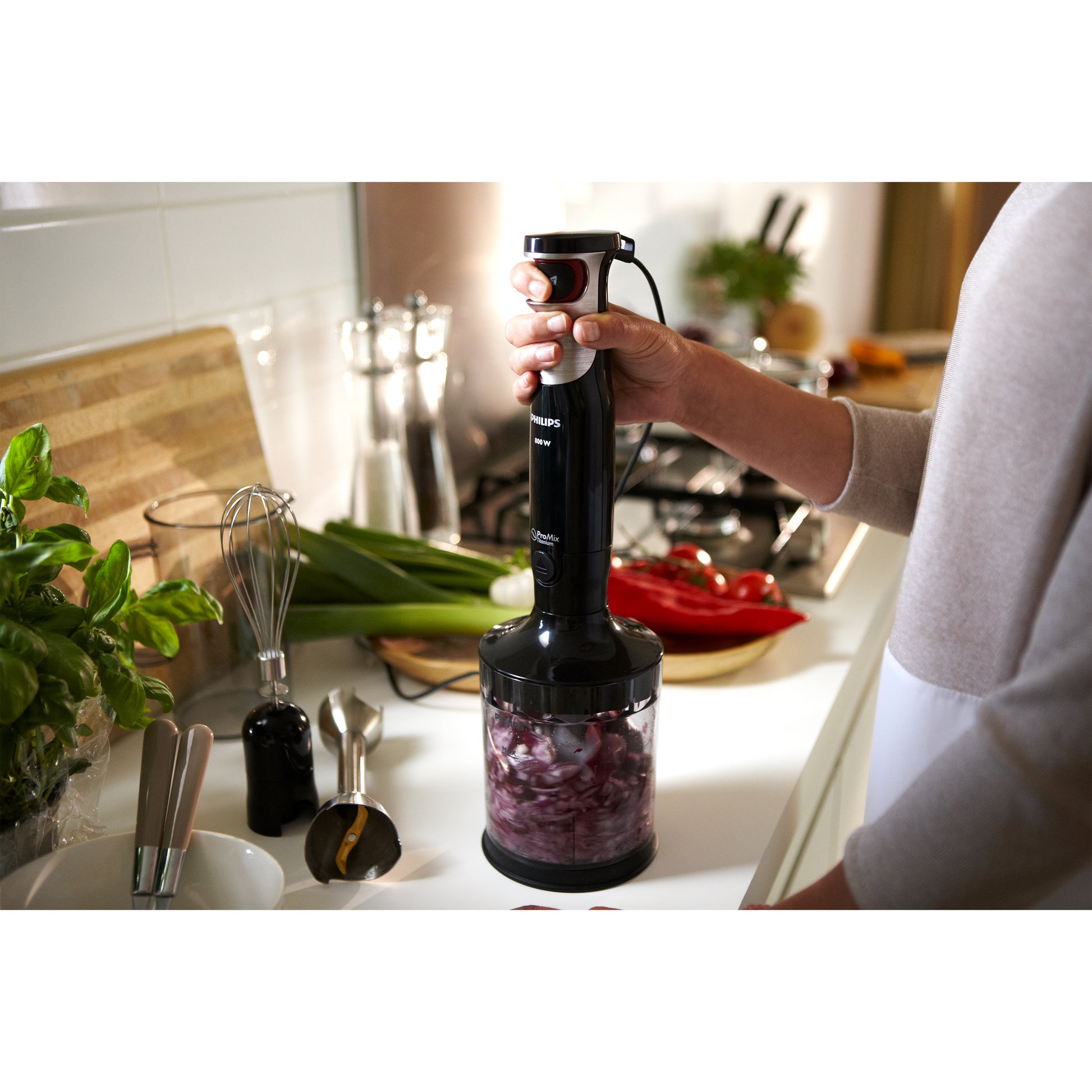 Person using a hand blender in a kitchen with ingredients on the counter.