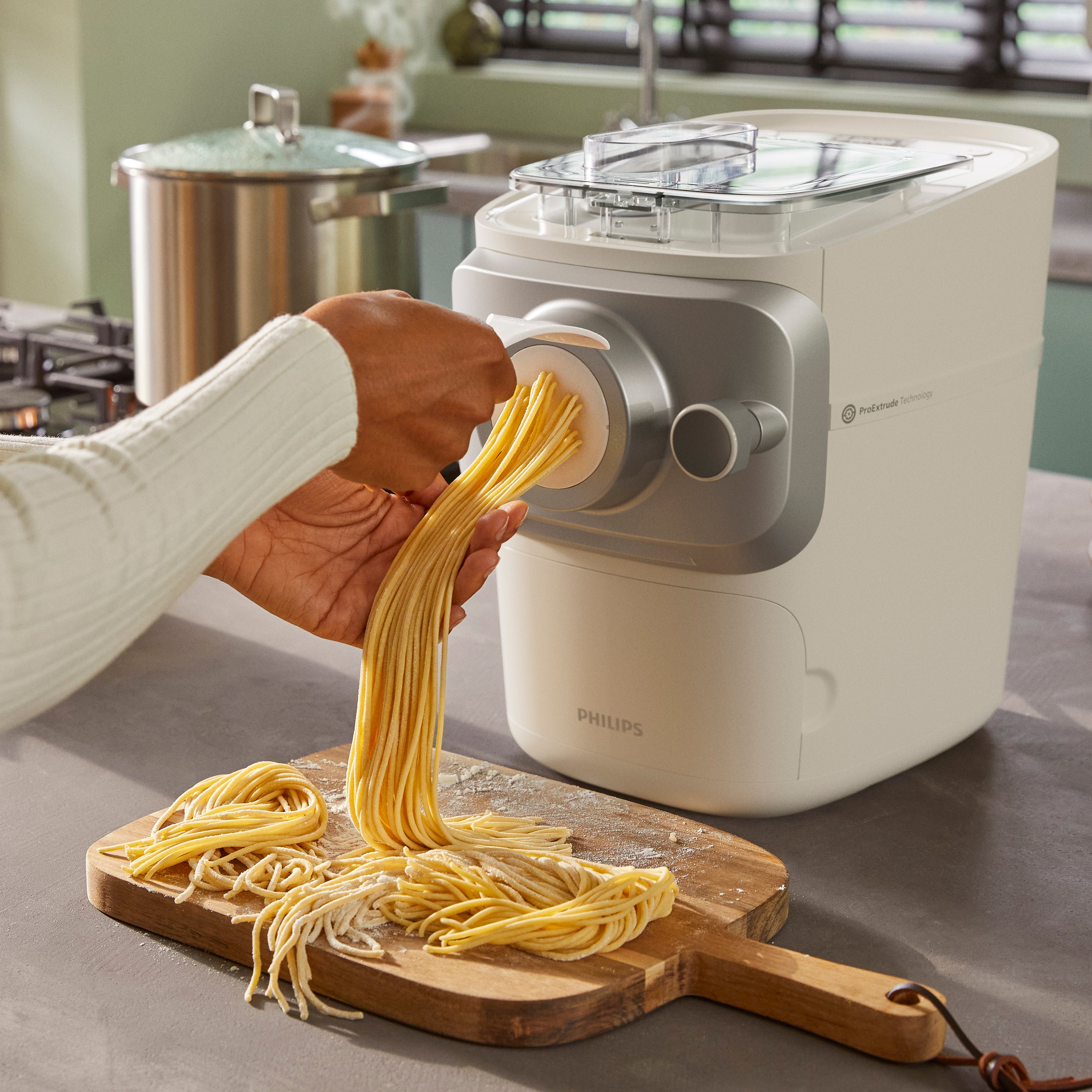 Person using a Philips pasta maker to make fresh pasta in a kitchen setting.
