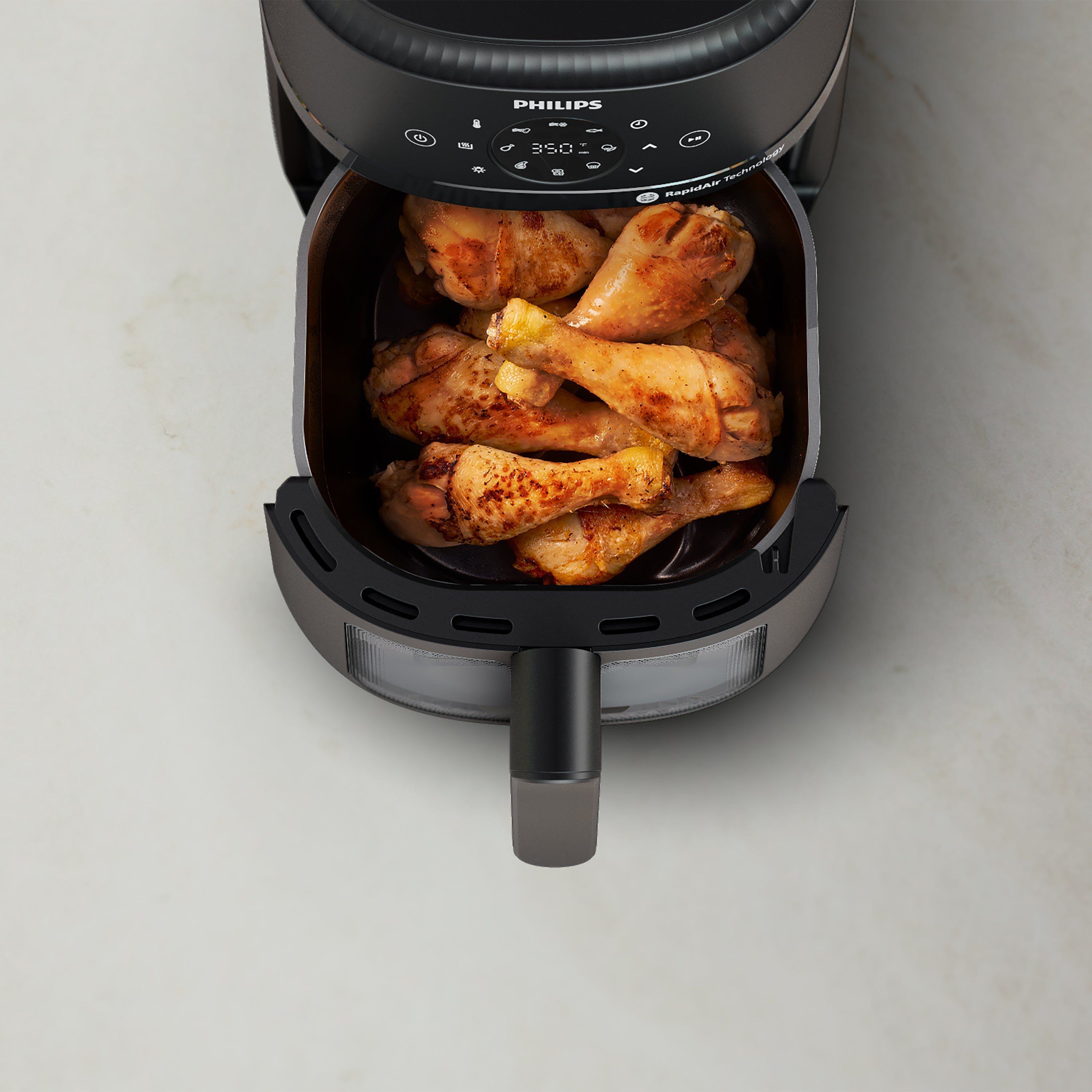 Philips air fryer with chicken legs inside on a light gray background