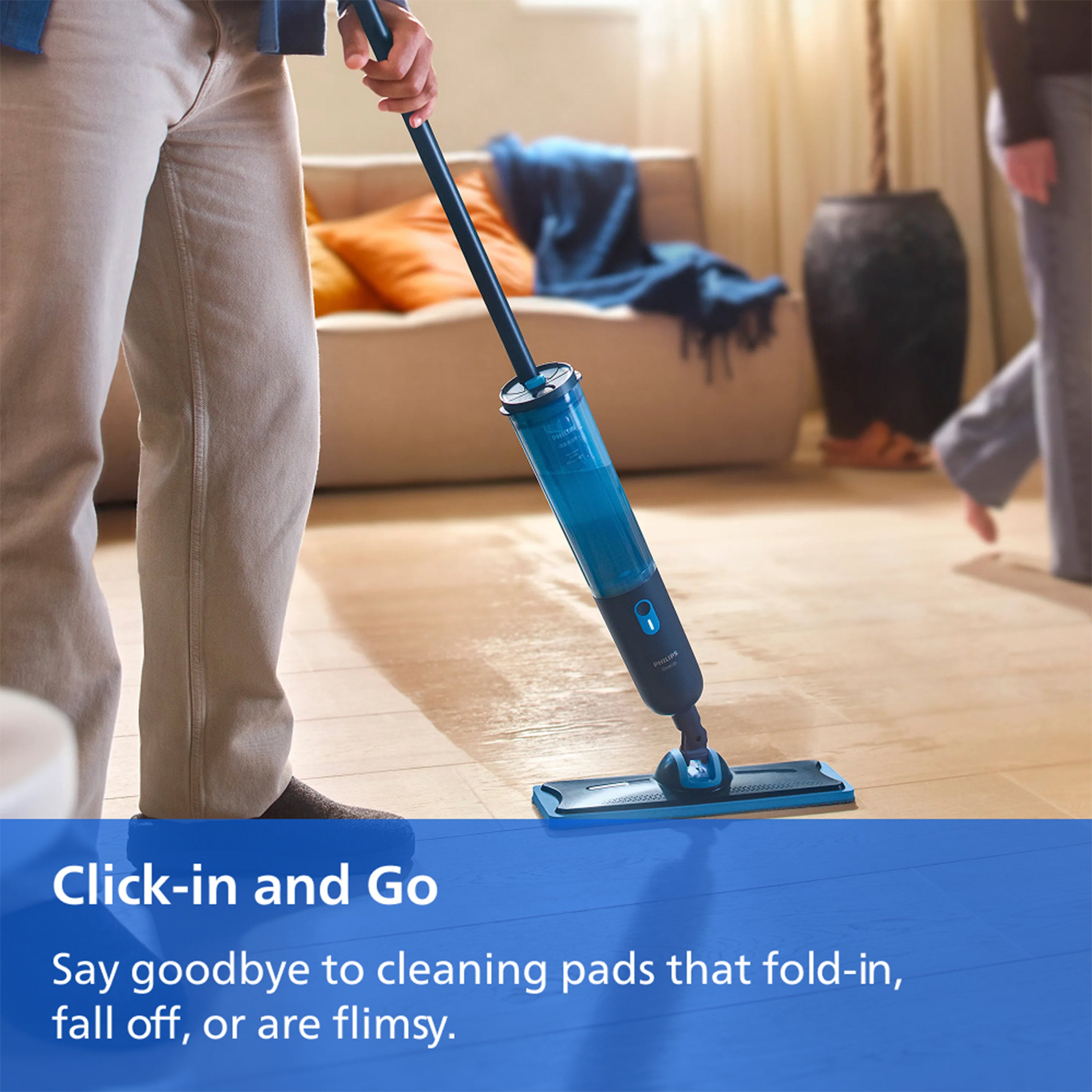 A person mops a light wood floor with a blue and black steam mop in a living room. A blue banner at the bottom reads 'Click-in and Go Say goodbye to cleaning pads that fold-in, fall off, or are flimsy.