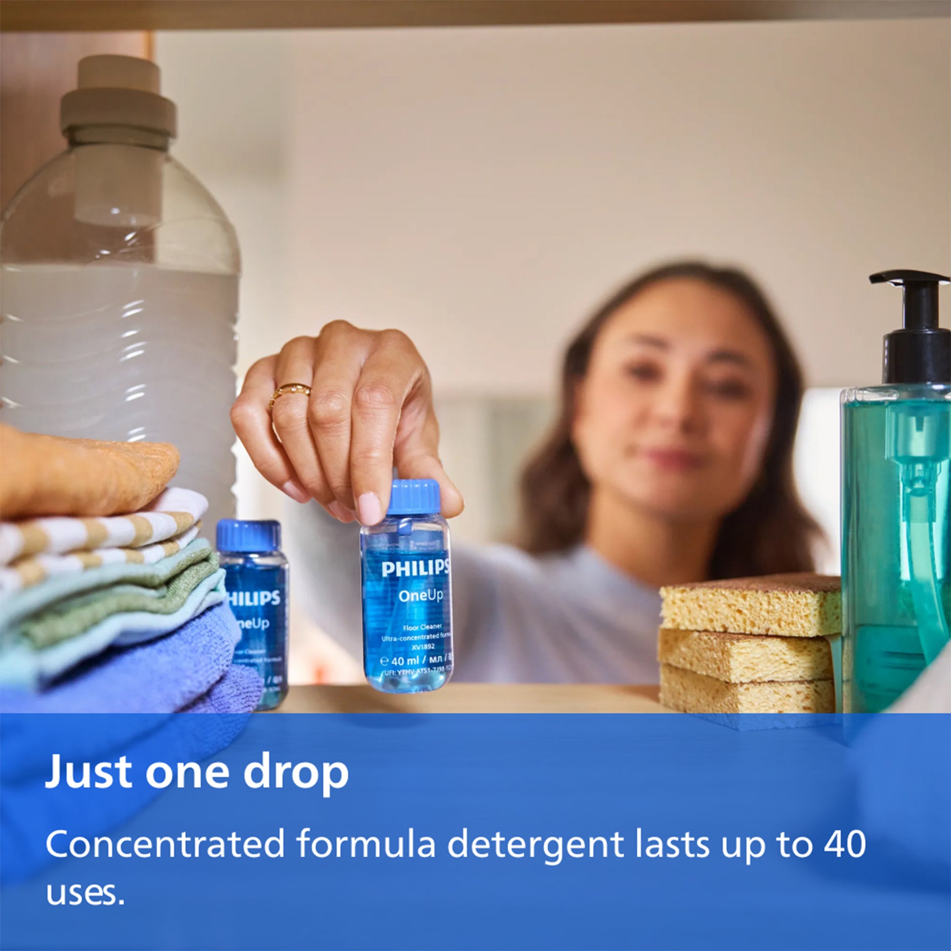 A woman holds a small blue bottle of PHILIPS OnCloud laundry detergent in a bright indoor setting, with folded towels, a large bottle, and a teal soap dispenser around her. A blue text banner at the bottom reads, 'Just one drop.