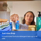 A woman holds a small blue bottle of PHILIPS OnCloud laundry detergent in a bright indoor setting, with folded towels, a large bottle, and a teal soap dispenser around her. A blue text banner at the bottom reads, 'Just one drop.